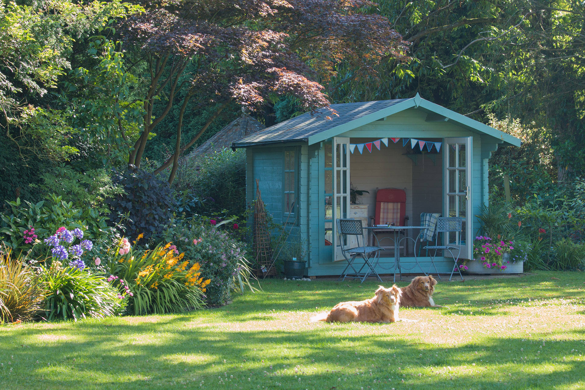 Gartenhäuser inkl. Service und Beratung + Aufbau finden Sie bei uns Gemütliches Gartenhaus mit Sitzecke, Hunde liegen auf der Wiese davor, im Garten